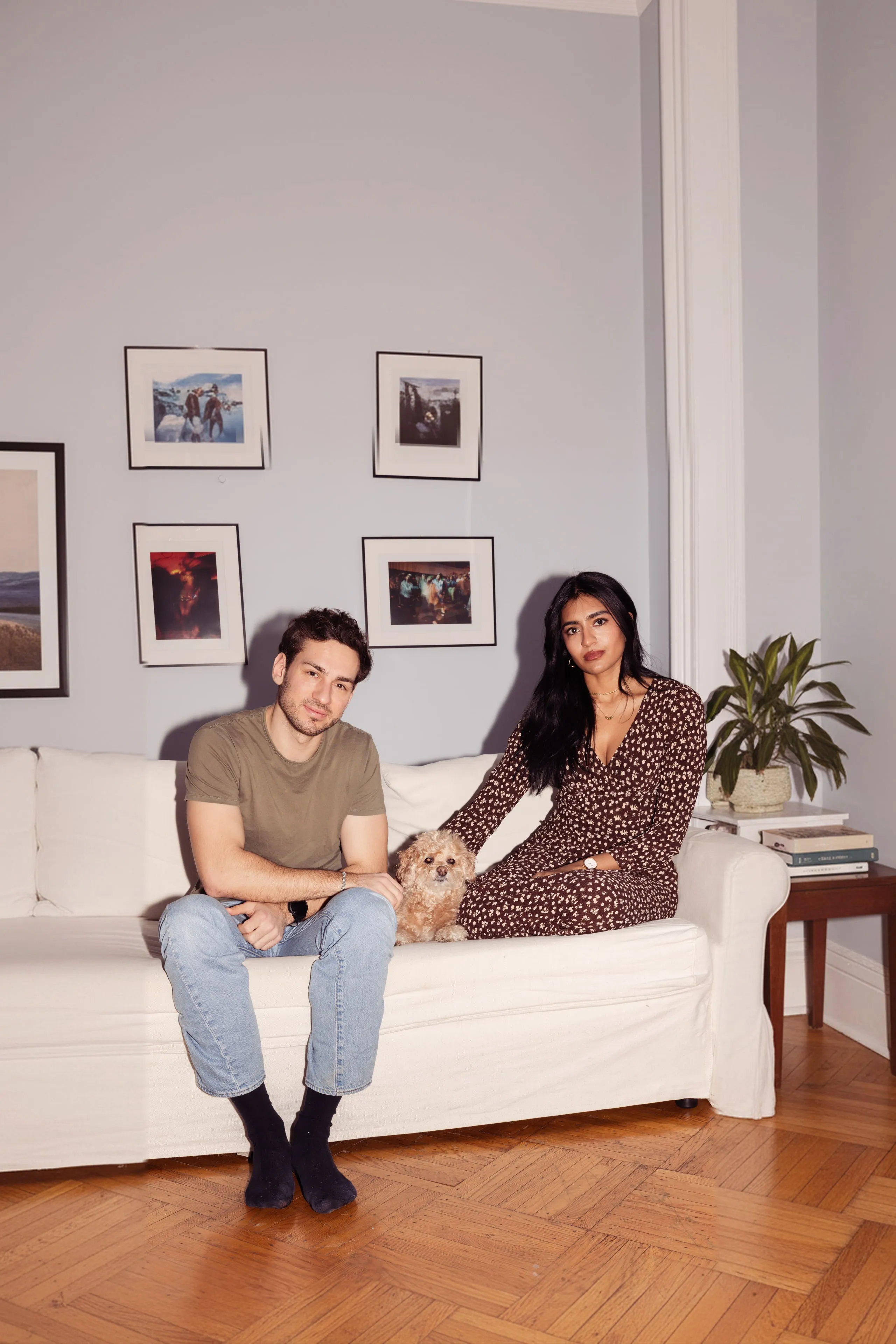 Founders Sindu and Jakob sitting on a couch at home with Omi, a small apricot poodle